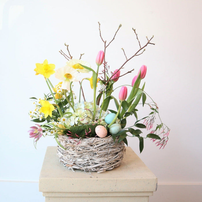 Easter Basket | A spring Easter arrangement with yellow, white, pink, green, and accent branches. The arrangement is in a basket with decorative pink and blue eggs.