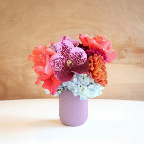 Fairy | Vased Arrangement | A blue vase with roses, mums, orchids, and hydrangea. Colors are pink, purple, and blue.