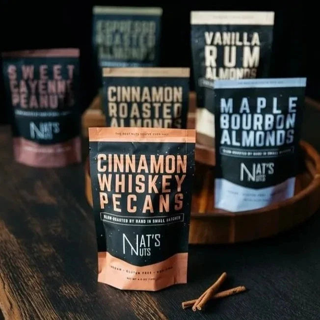 Nat's Nut's Assorted | Nat's Nuts | 6 bags of nuts against a dark background. Sweet cayenne Peanuts, espresso roasted almonds, vanilla rum almonds, cinnamon roasted almonds, maple bourbon almonds, cinnamon whiskey pecans.