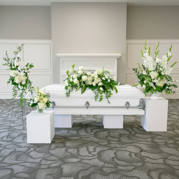 White casket with floral arrangements in a funeral home setting