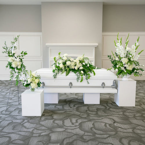 White casket with floral arrangements in a funeral home setting